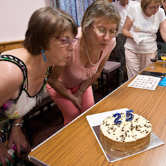 Marian and Sue blowing the candles out after cutting the cake.